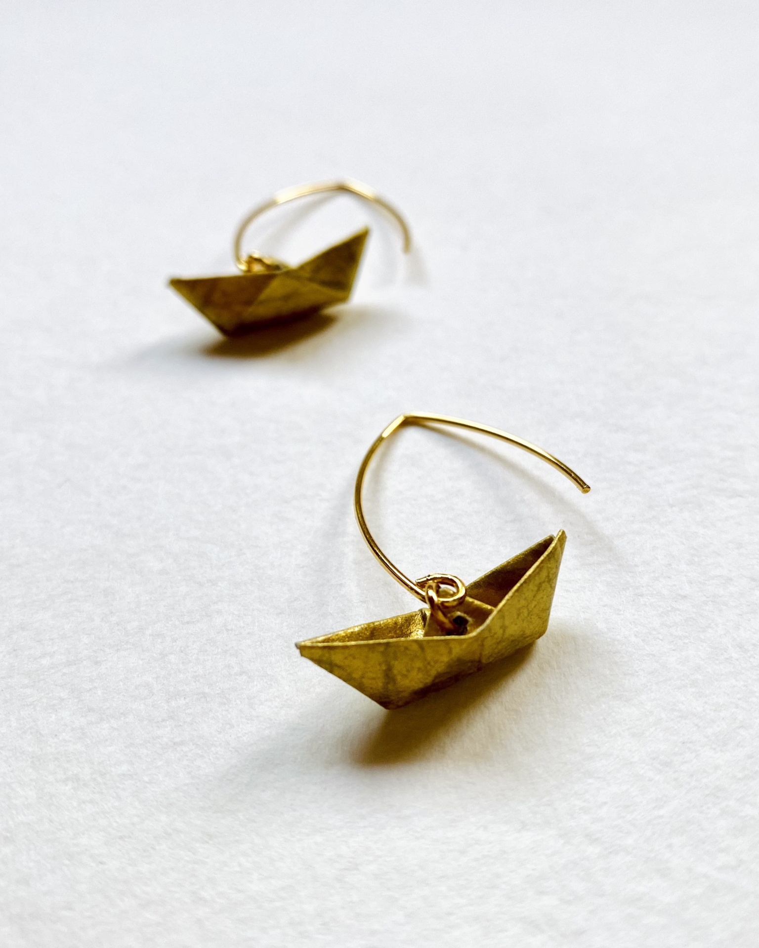 Brincos Boto Brincos dourados em forma de barco de papel sobre fundo branco.