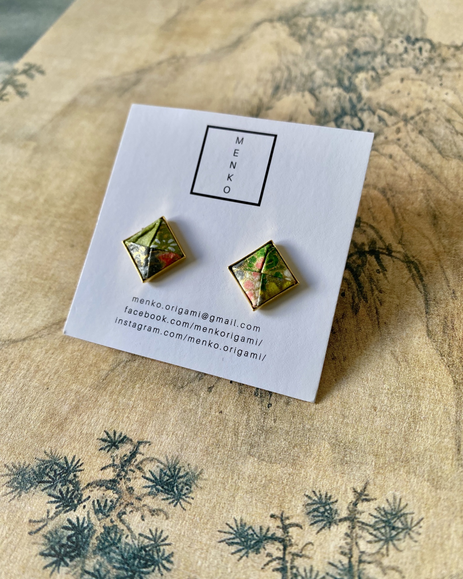 Brincos Menko Clássico Par de brincos quadrados origami com padrão floral em cartão branco.