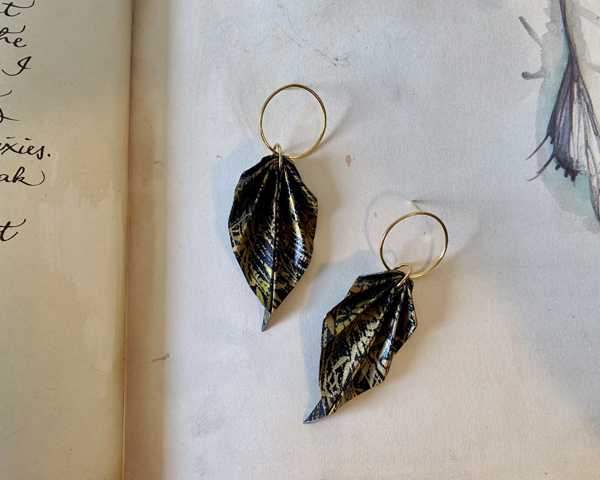 Brincos Folha Brincos dourados com pendentes em forma de folhas pretas com detalhes dourados