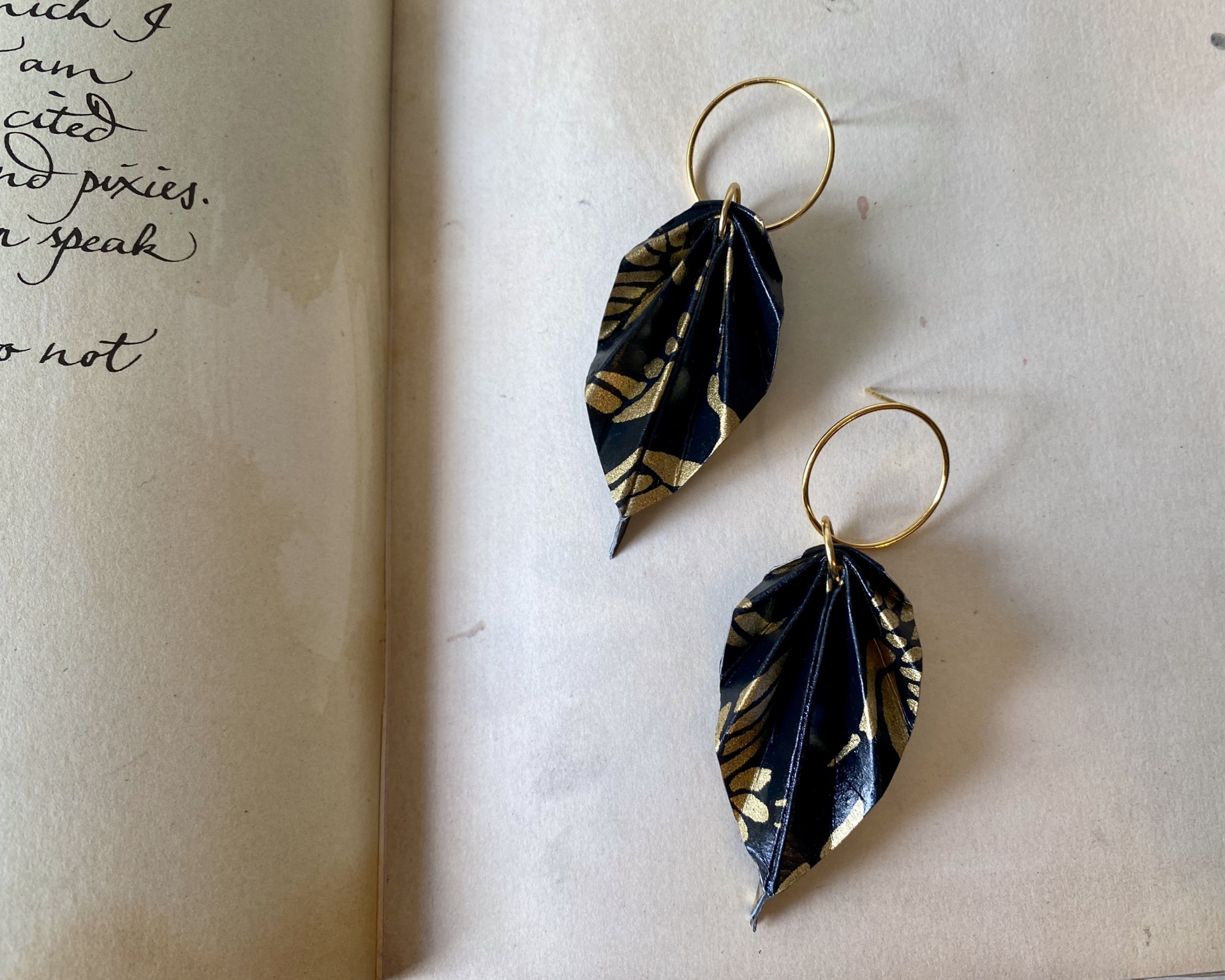 Brincos Folha Brincos em forma de folha negros com desenhos dourados e argolas douradas.