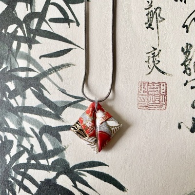 Colar com pendente de tecido colorido pendurado sobre papel com desenhos e caligrafia chinesa