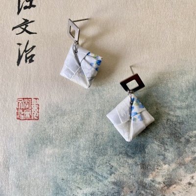 Brincos quadrados em tecido floral azul e base metálica sobre fundo asiático