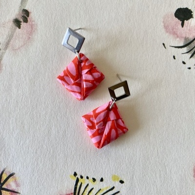 Brincos com base metálica e pendentes em tecido rosa e vermelho sobre papel floral