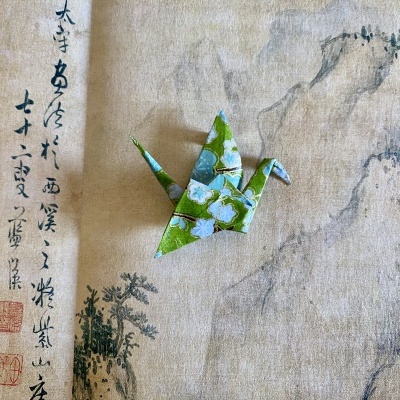 Origami de pássaro em papel floral azul e verde sobre papel com gravura asiática e texto em caracteres chineses