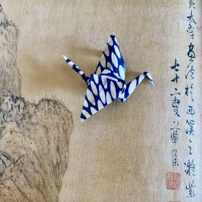 Origami de garça azul e branco sobre pano com pintura e escrita oriental
