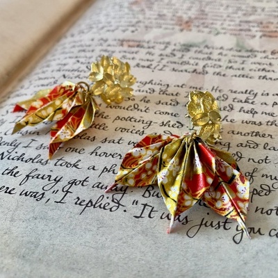 Brincos dourados com pendentes de tecido floral sobre página escrita à mão