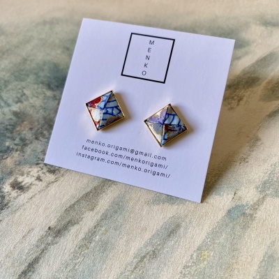 Brincos quadrados coloridos com moldura dourada em cartão branco com logótipo MENKO e contactos.