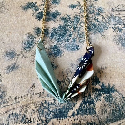 Colar com pendentes de tecido azul claro e floral em fundo estampado de paisagem.