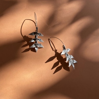 Brincos prateados em forma de folhas sobre fundo castanho claro