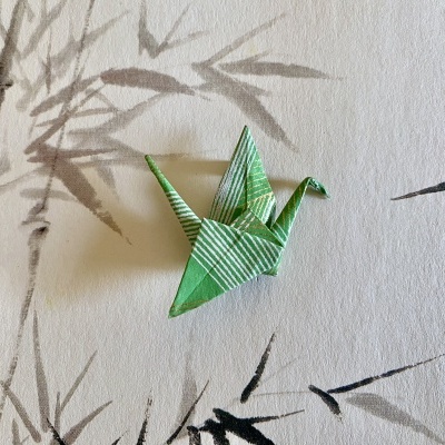 Origami de pássaro verde com detalhes brancos e dourados sobre papel de parede com desenhos de bambu