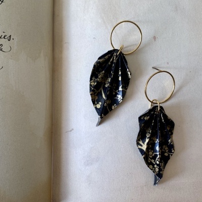 Brincos em forma de folha em tecido preto com padrão dourado floral e argolas douradas