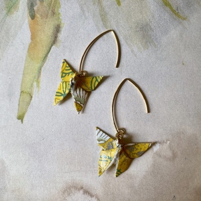 Brincos com pendente origami amarelo e argola dourada sobre fundo de papel aquarelado