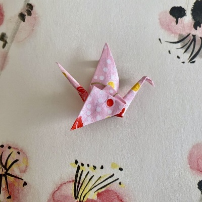 Origami de pássaro em papel rosa com bolinhas e pontos coloridos sobre fundo branco floral
