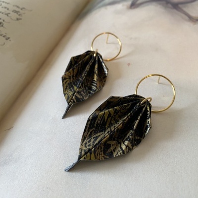 Brincos com argolas douradas e pendentes em forma de folhas preto e dourado sobre página de livro aberto