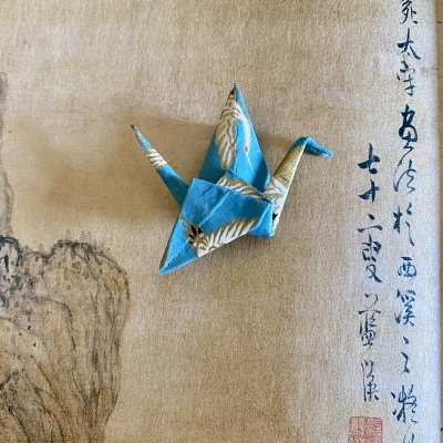 Gralha de origami azul com padrão de gruas douradas sobre papel com caracteres asiáticos