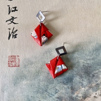 Brincos com pendentes de papel colorido e base de metal sobre fundo com escrita asiática