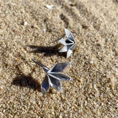 Brincos de metal prateado em forma de folhas sobre areia da praia