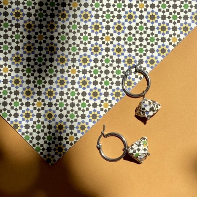 Brincos de argola com pendentes cerâmicos coloridos sobre superfície castanha e padrão de azulejos