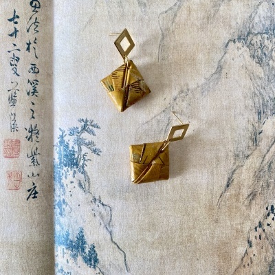 Brincos com pendentes de tecido amarelo e argola dourada sobre pano com escrita e desenho asiático