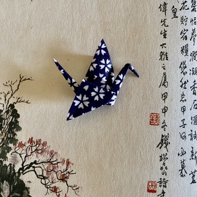 Grulla origami azul com flores brancas sobre papel com pintura e caligrafia chinesa.