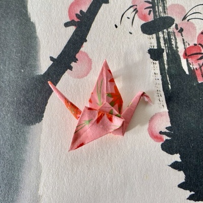 Cisne de origami rosa com padrão de folhas sobre papel decorativo em preto e rosa