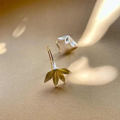 Brincos prateados em forma de folhas sobre superfície bege clara