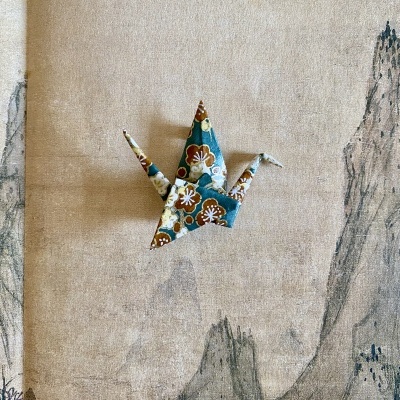 Grua de origami com padrão floral sobre tecido bege com desenho de montanhas