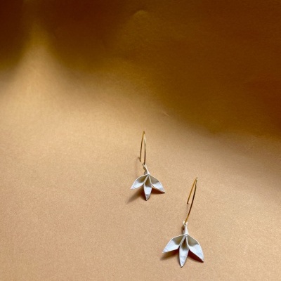 Brincos dourados com pendente prateado em forma de folhas sobre fundo castanho claro