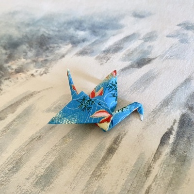 Pássaro de origami azul com padrões coloridos sobre superfície cinza