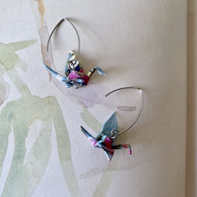 Brincos de pássaros de papel colorido com alças metálicas sobre fundo pintado