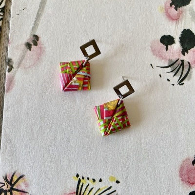Brincos quadrados coloridos sobre fundo branco com flores.