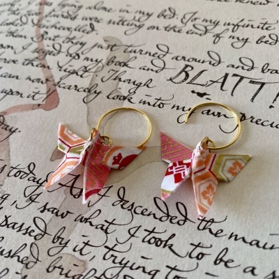 Brincos com borboletas de papel colorido sobre papel com texto manuscrito