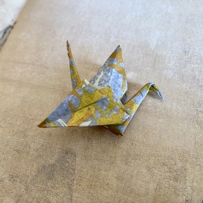 Origami de garça azul e dourado sobre superfície bege