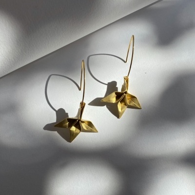 Brincos dourados em forma de flores sobre fundo branco com sombras