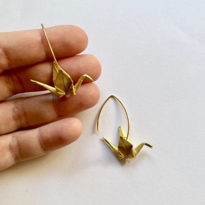 Brincos dourados em forma de gruás origami sobre fundo branco.