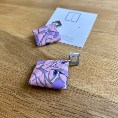 Brincos quadrados lilás com padrão floral e gancho metálico sobre mesa de madeira