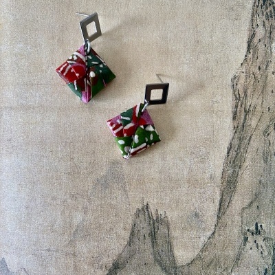 Par de brincos com base em metal prateado e pendente triangular em tecido colorido.