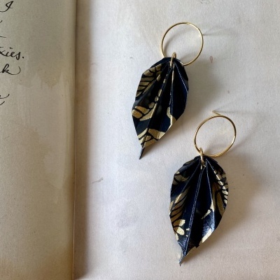 Brincos em forma de folha negros com desenhos dourados e argolas douradas.