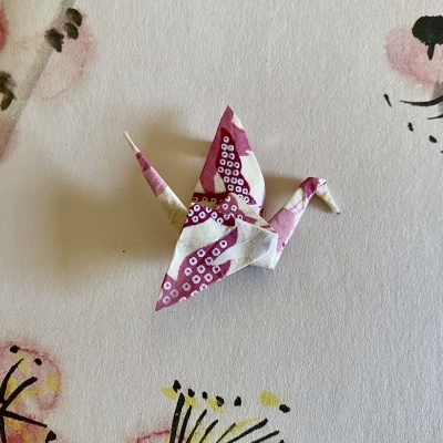 Origami de pássaro em papel rosa e creme com padrão circular sobre fundo com padrão floral.