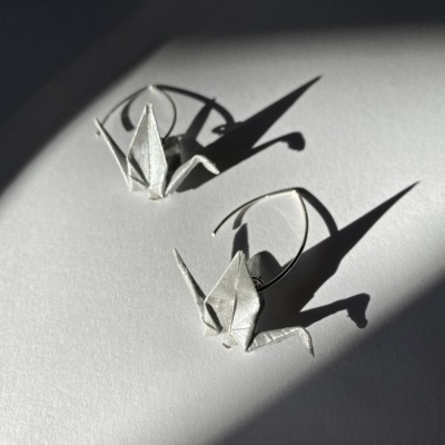 Brincos de origami em forma de gruas sobre fundo branco com sombras.