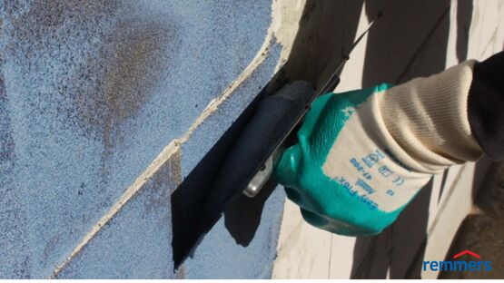 REMMERS MB1K Mão com luva a aplicar tinta preta em parede azul