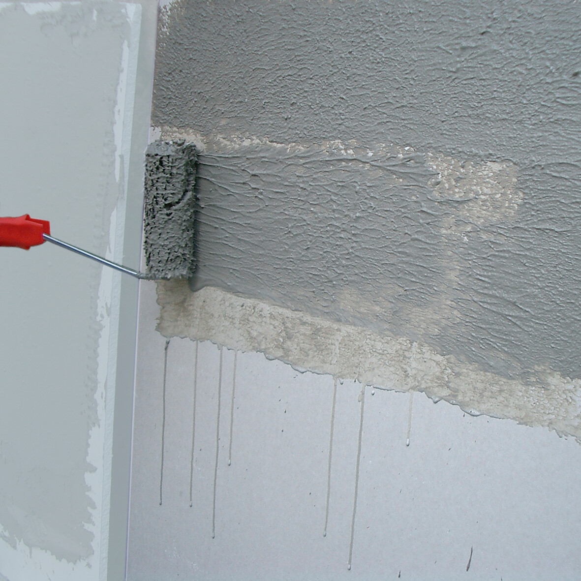 OTTOFLEX® - Argamassa de Impermeabilização Rolo de pintura a aplicar tinta cinzenta numa parede