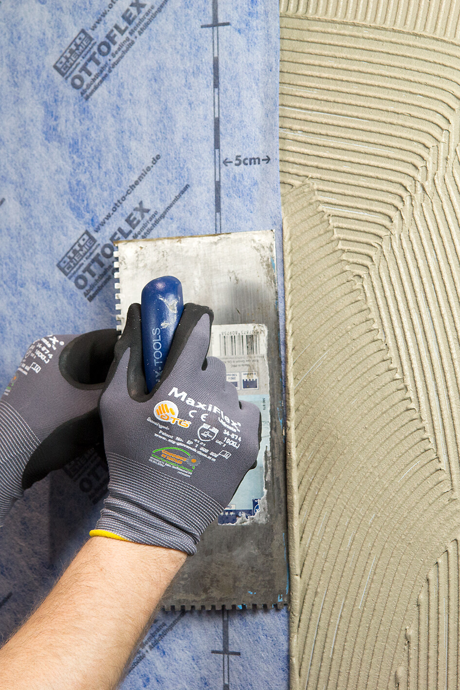 OTTOFLEX® - Tela de Impermeabilização Mãos com luvas a usar talocha em superfície texturada para azulejos
