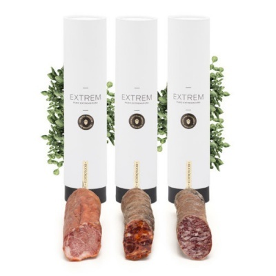 Três linguiças embaladas em cilindros brancos com texto EXTREM e selo dourado.