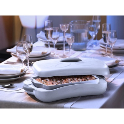 Recipiente branco com lasanha numa mesa posta com pratos e copos claros