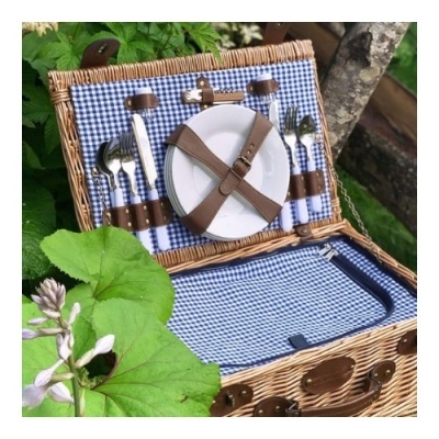 Cesto de piquenique aberto com interior azul e branco aos quadrados, talheres, pratos brancos e tiras de couro castanho