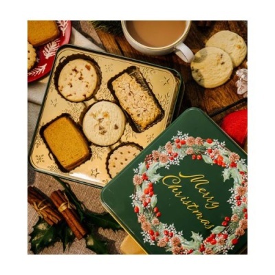 Lata verde decorativa com texto 'Merry Christmas' e biscoitos variados numa mesa festiva