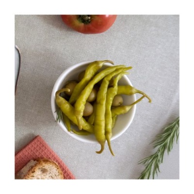 Pimentos verdes num recipiente branco com tomate, alecrim e pão em fundo claro