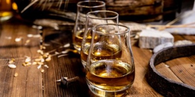 Três copos com whisky sobre mesa de madeira rústica