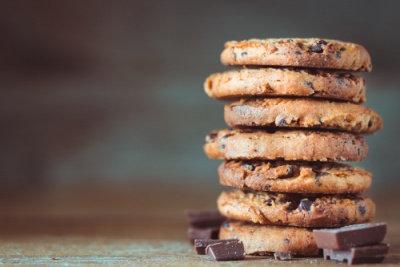 Pilha de bolachas com pedaços de chocolate e pedaços de chocolate ao redor sobre superfície de madeira